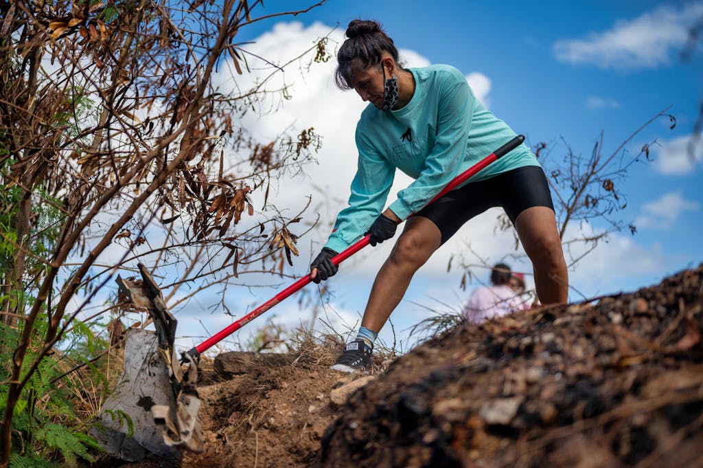 Woman volunteering in an outdoor cleanup effort, removing debris with a shovel.